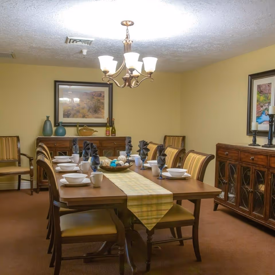 Well-lit dining room with a long wooden table set for eight, striped chairs, sideboards and framed artwork on the walls.