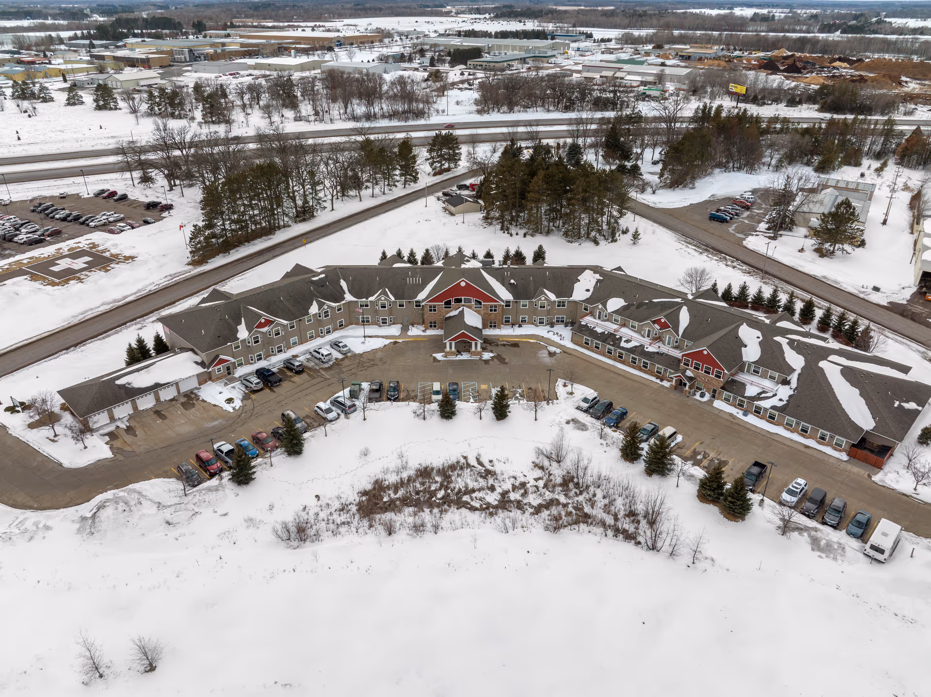 Aerial view of a curved senior living facility building with parked cars and snow-covered grounds.