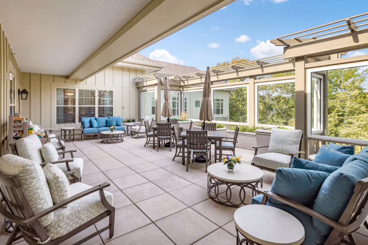 Covered outdoor patio with lounge seating, dining tables and umbrellas, and blue-cushioned chairs overlooking trees.