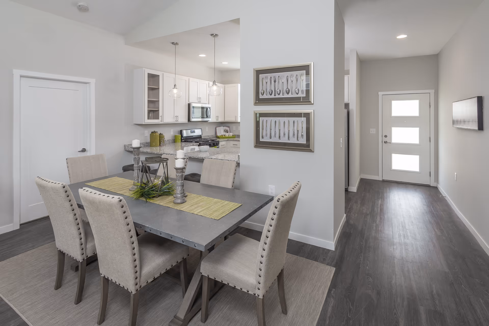 Dining area with a modern table and upholstered chairs adjacent to an open kitchen and front entry hallway.