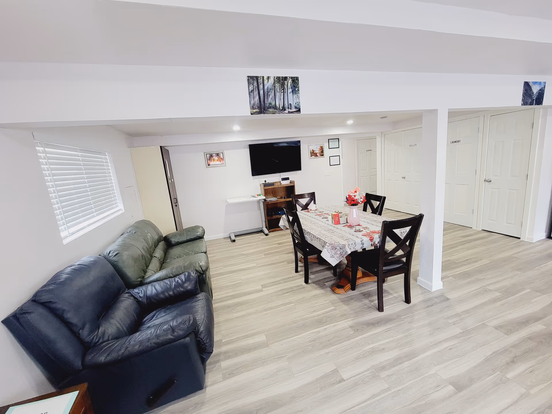 Open common room with a couch, dining table set with flowers, a wall-mounted TV, and doors along the back wall.