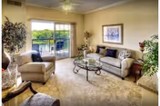 Bright living room with a sofa, armchairs, glass coffee table and sliding glass door opening to a balcony with greenery.