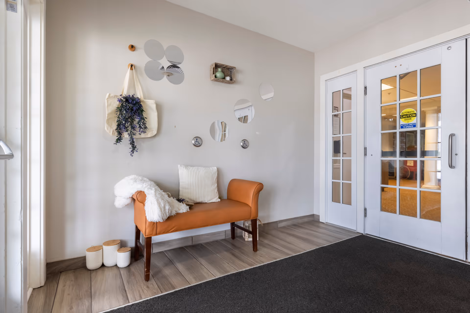Small entry seating area with an orange bench, decorative wall mirrors, potted accents and double glass doors.