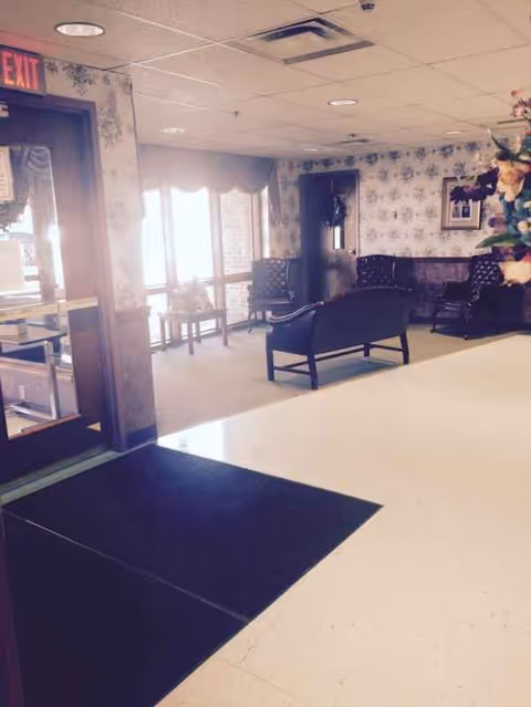 Nella's Nursing Home lobby with seating, floral wallpaper, windows, and exit sign.