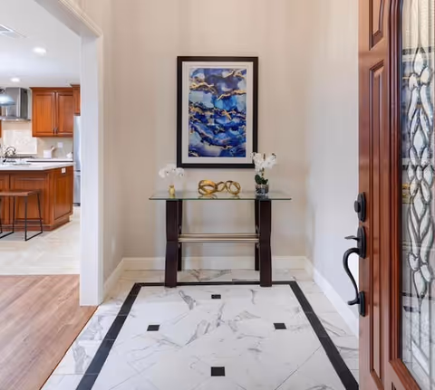 Foyer area with glass console table, framed artwork, flowers, and decor near a front door.