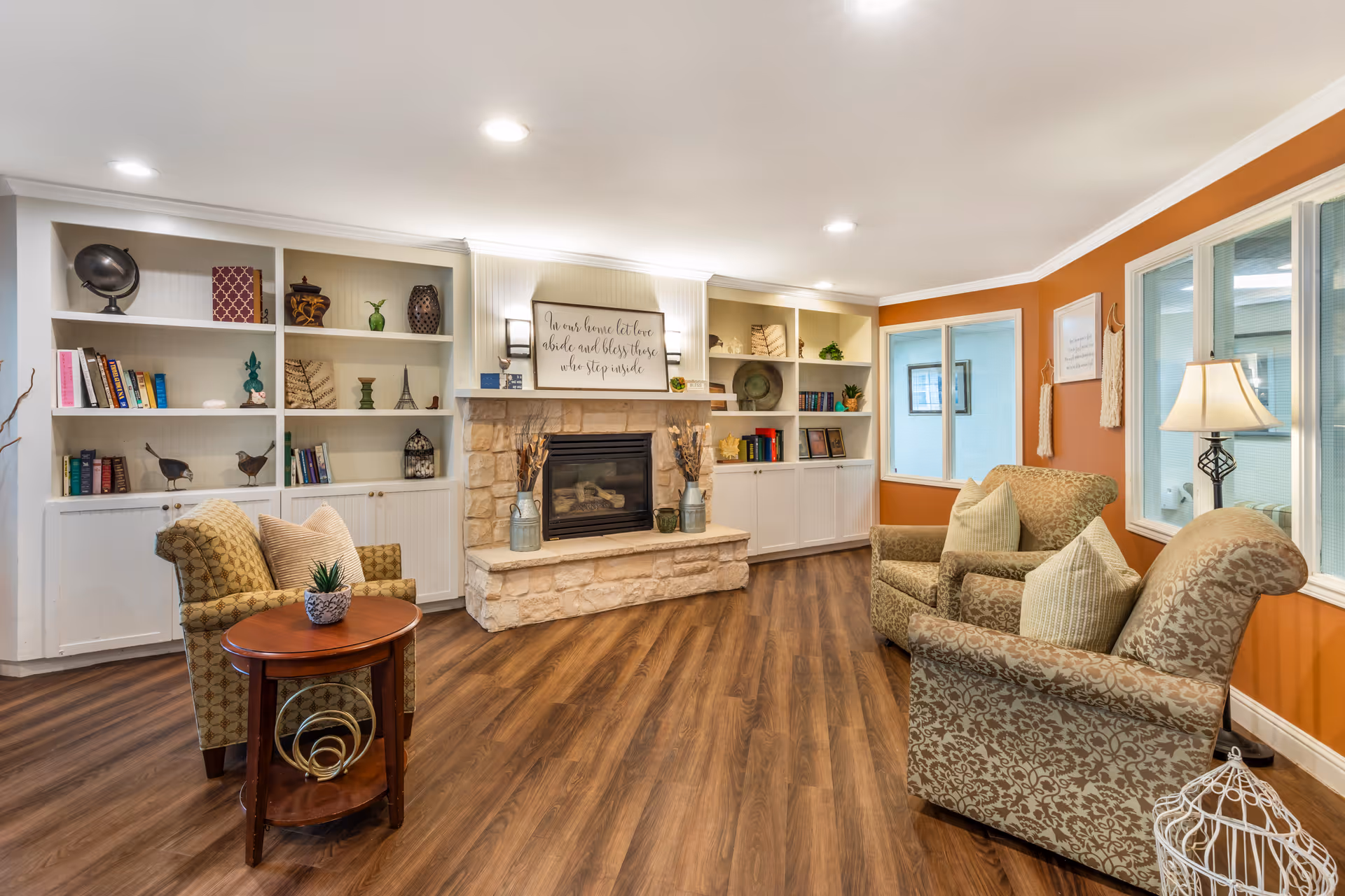 Cozy living room with armchairs arranged around a stone fireplace, built-in bookshelves, and wood flooring.