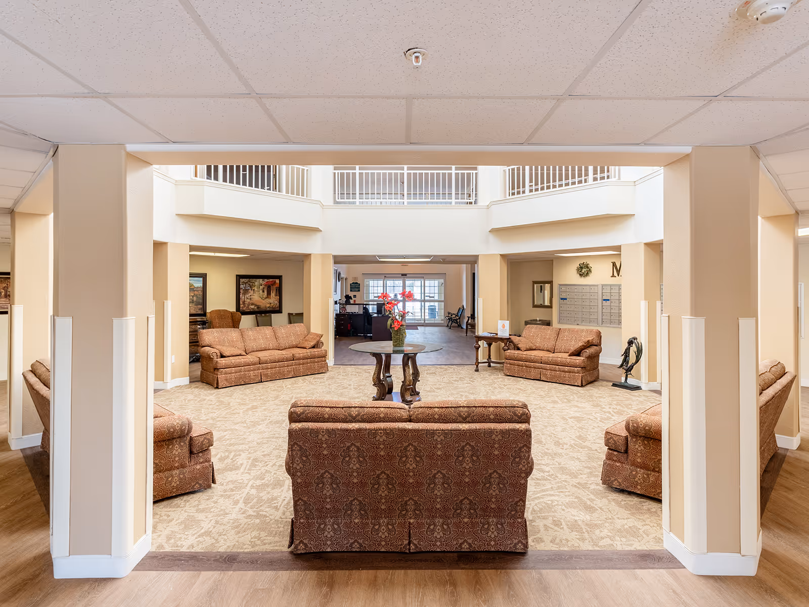 Spacious senior living common area with multiple upholstered sofas arranged around a central table beneath a two-story atrium.