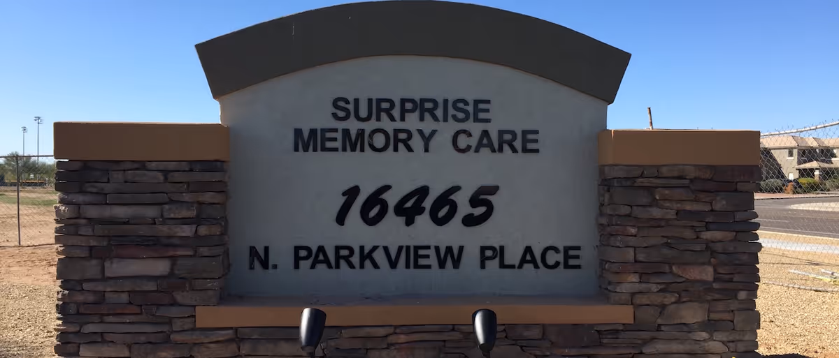Stone and stucco entrance sign reading "Surprise Memory Care 16465 N. Parkview Place" against a clear blue sky.