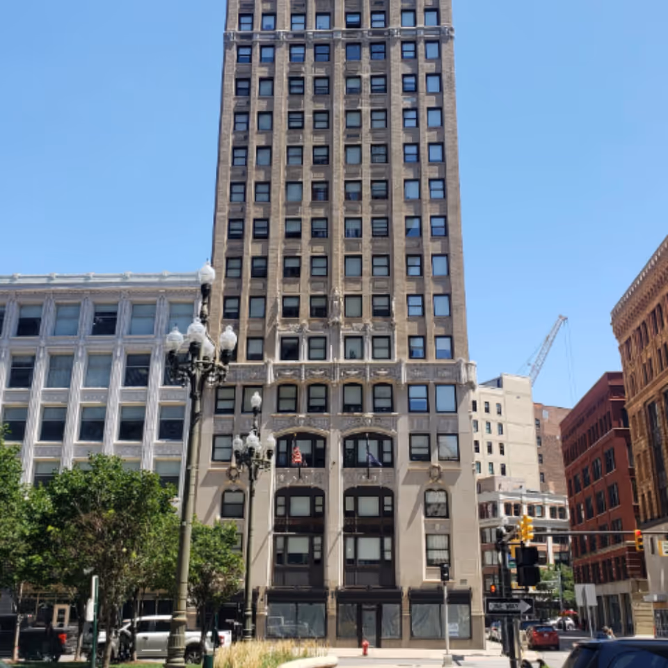 Tall historic multi-story apartment building facade on a city street with ornate details, street lamps, and neighboring buildings under a clear blue sky.