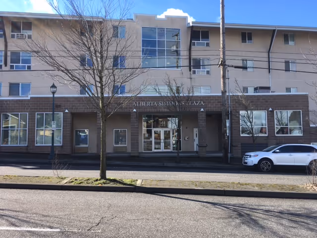 Exterior front view of the Alberta Simmons Plaza building showing the main entrance, windows, and a parked white SUV.