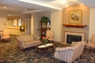 A cozy community lounge with striped sofas and armchairs arranged around a coffee table and fireplace.