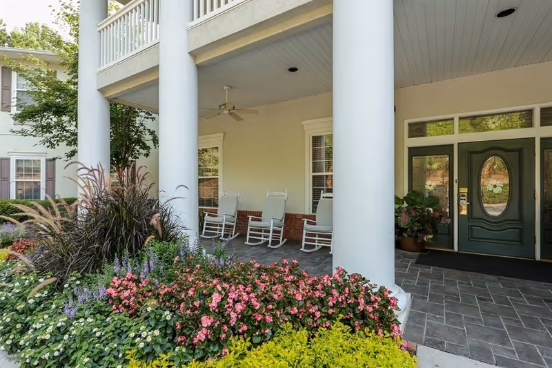 Covered front porch with white columns, rocking chairs, and colorful flowers at the Oaks at Stockbridge.
