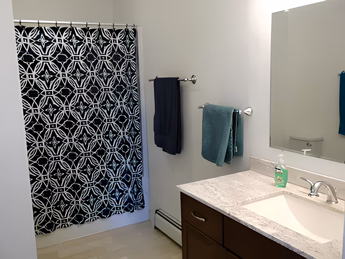 Bathroom with a patterned black-and-white shower curtain, vanity with sink and mirror, and towel racks with hanging towels.