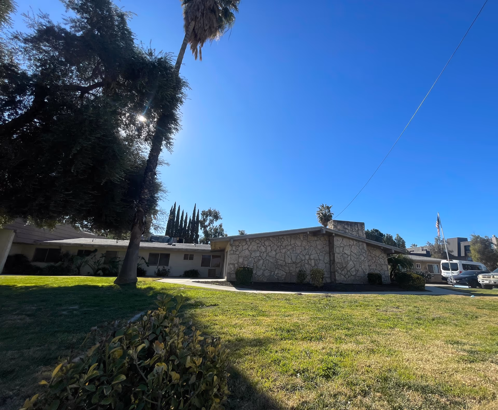 One-story stone-faced building with a lawn, trees, and a clear blue sky.