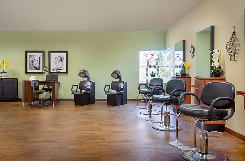 Open salon area with styling chairs, hooded hair dryers, mirrors and a desk against a light green wall.