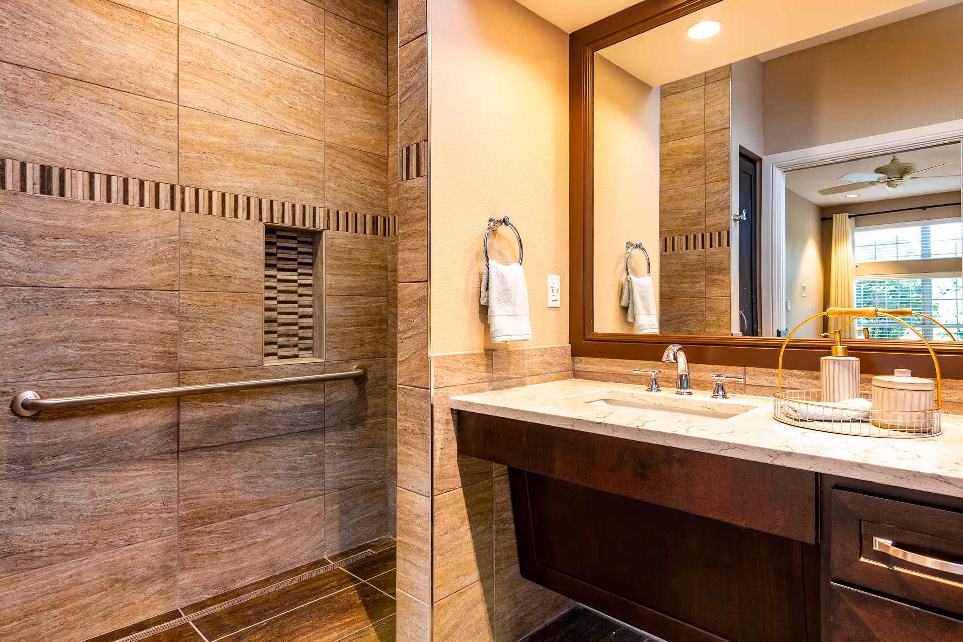 Modern accessible bathroom with a tiled walk-in shower and grab bar, marble-top vanity, sink and large mirror.