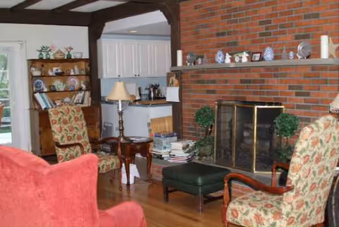 Cozy living room with brick fireplace, shelves, and floral upholstered chairs.