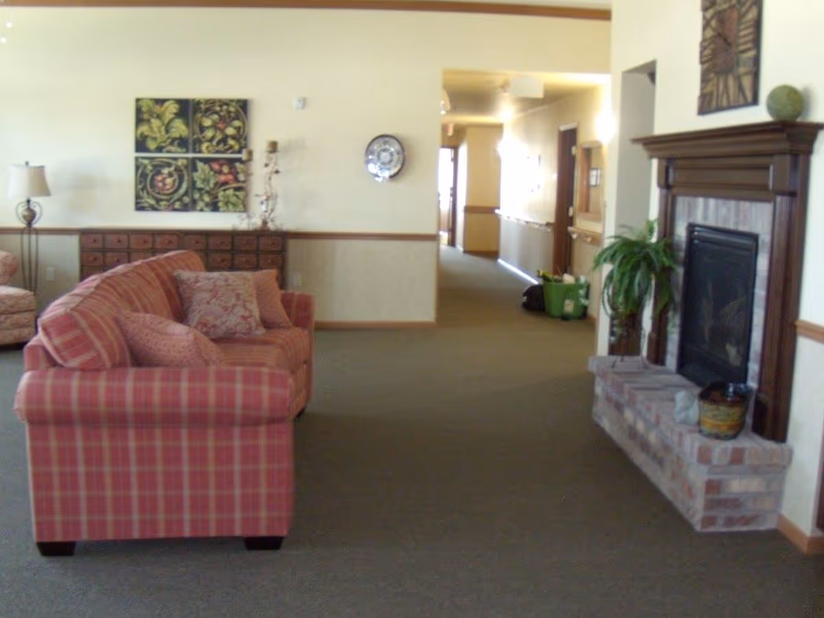 A common living area with a plaid sofa, fireplace, decorative wall art, and a hallway leading to rooms.