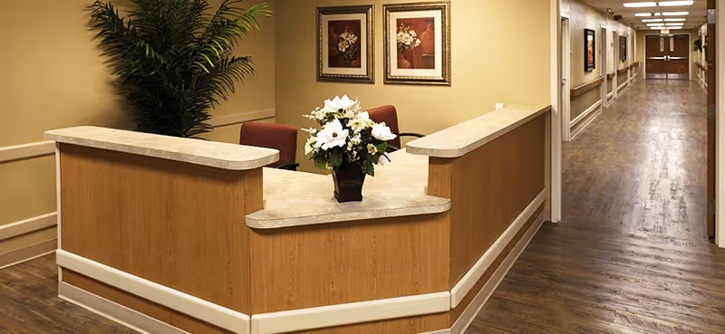 Reception desk with a vase of flowers beside a long hallway in a healthcare facility interior.
