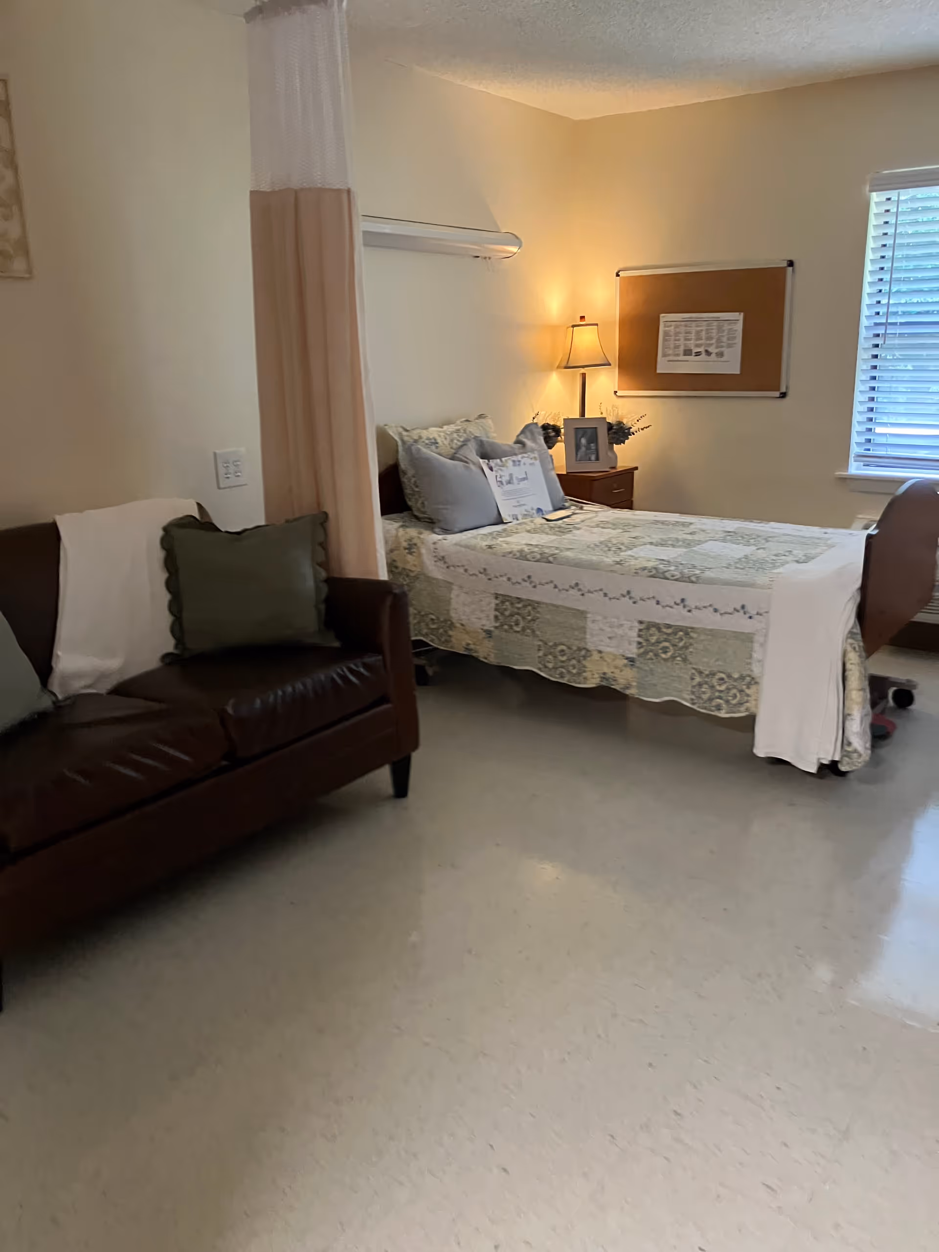A cozy bedroom with a bed, sofa, nightstand, lamp, and window.