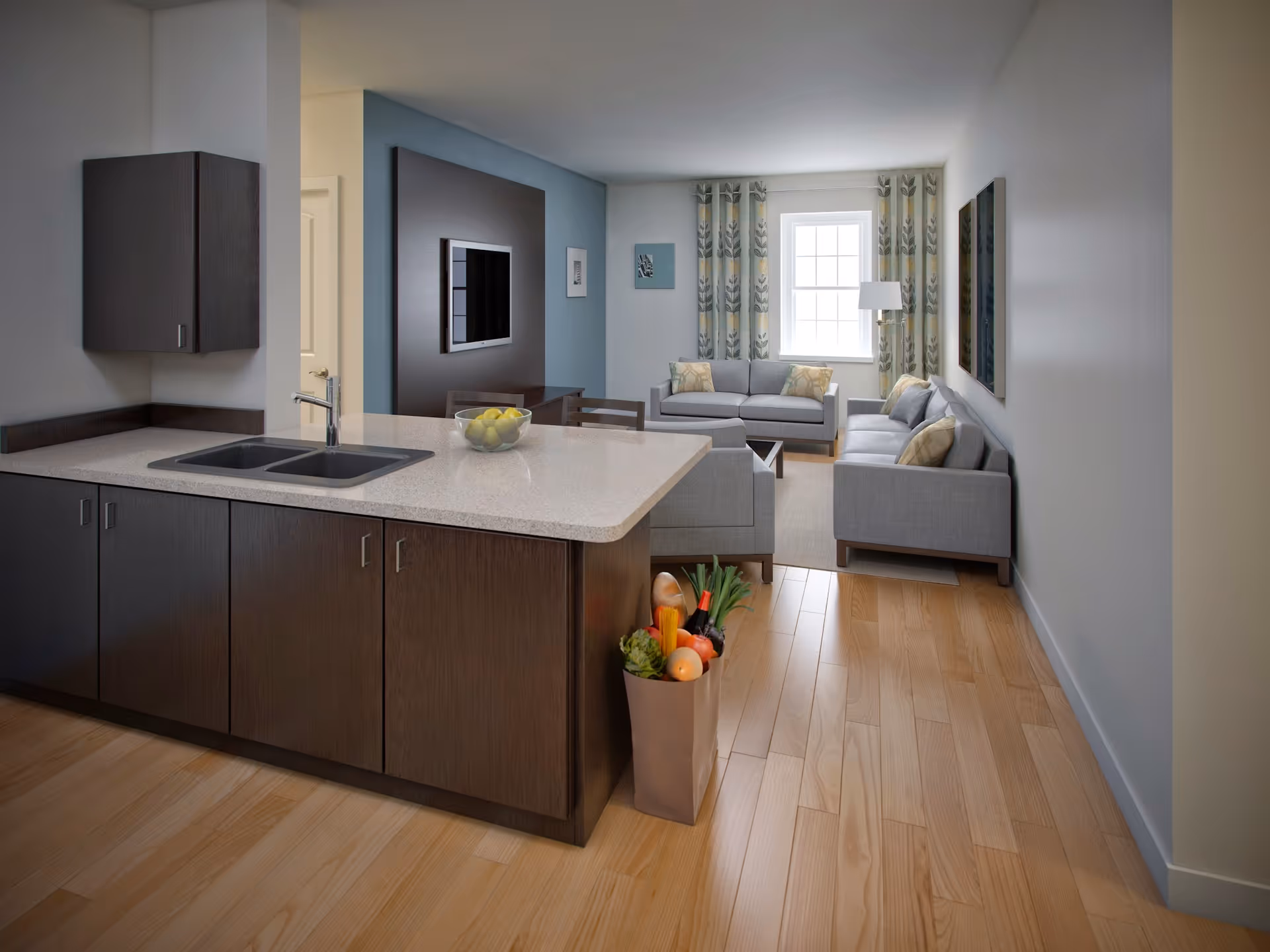 Open-plan interior showing a modern kitchen island with sink in the foreground and a bright living room with sofas and a window in the background.