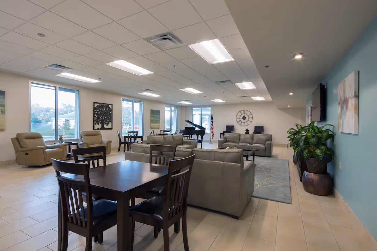 Spacious bright common lounge with sofas, armchairs, dining tables, a piano, and large windows.
