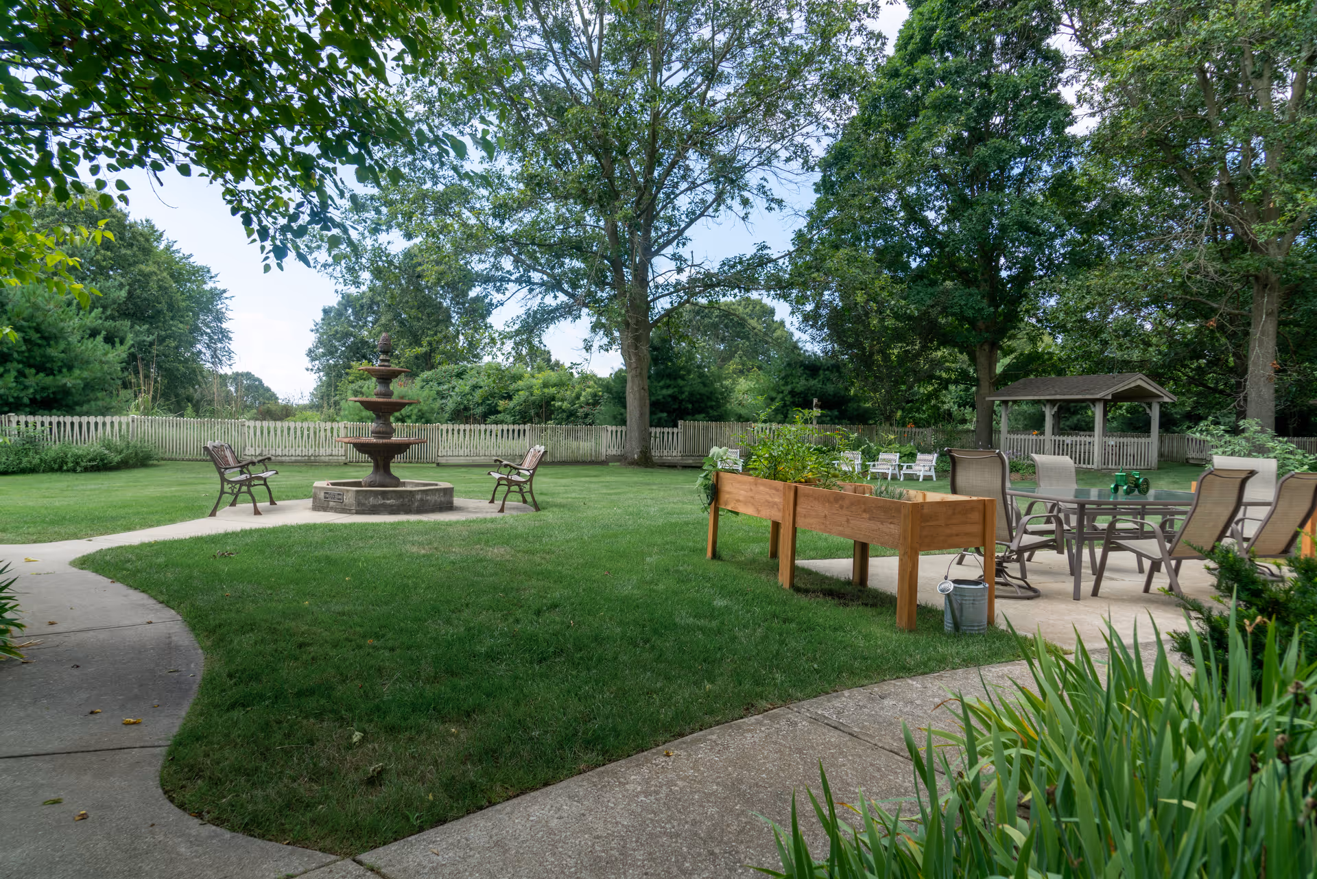 Well-maintained outdoor courtyard with a tiered fountain, benches, raised planters, and patio seating under large trees.