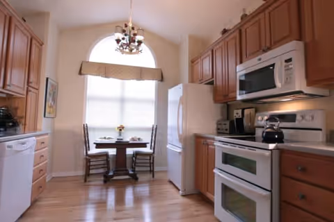 Bright kitchen with wooden cabinets, white appliances, and a small dining table by an arched window.