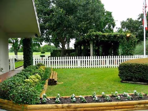 Well-kept outdoor yard with white fence, hedges, and a shaded gazebo.