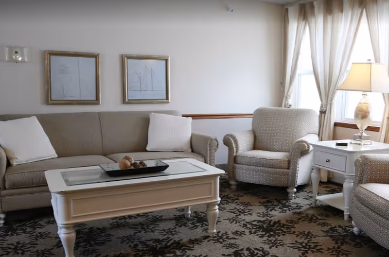 Comfortable living room with a sofa, two armchairs, a white coffee table, side table with a lamp, and framed wall art.