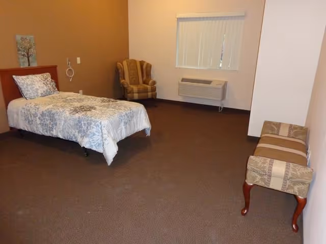 A furnished senior living bedroom with a bed, chair, and bench.