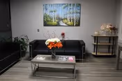 A modern nursing facility lounge with black sofas, glass coffee table, and wall art.