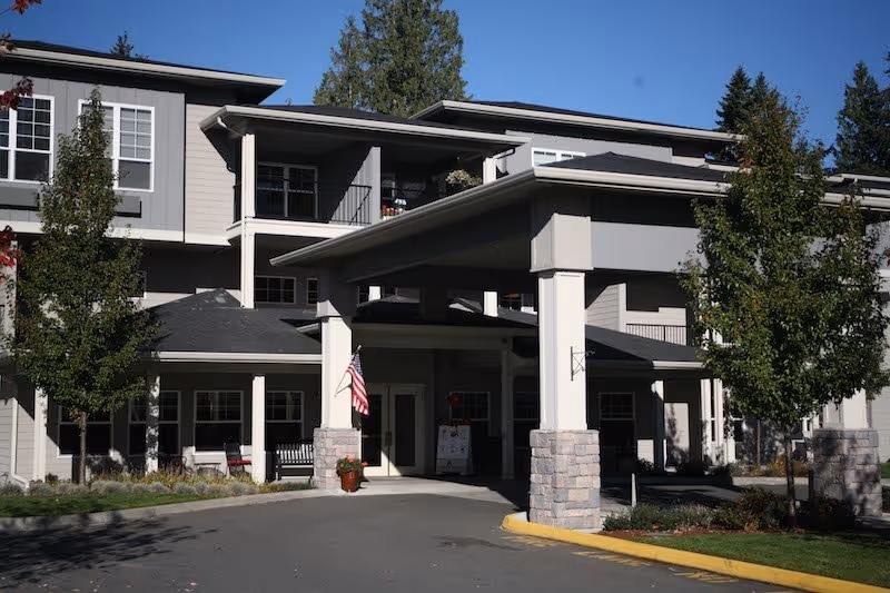 Exterior view of a multi-story senior living facility entrance with flag and covered drop-off.