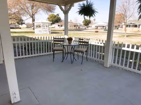 Covered outdoor patio with table and chairs, white fencing, gazebo in the background.