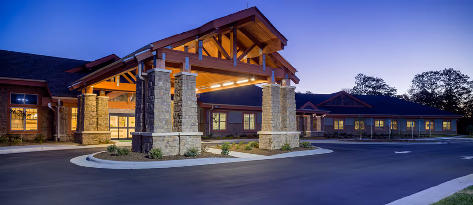 Exterior view of The Foley Center at Chestnut Ridge at dusk, showing a large covered entrance supported by stone pillars with warm interior lights visible through the windows.