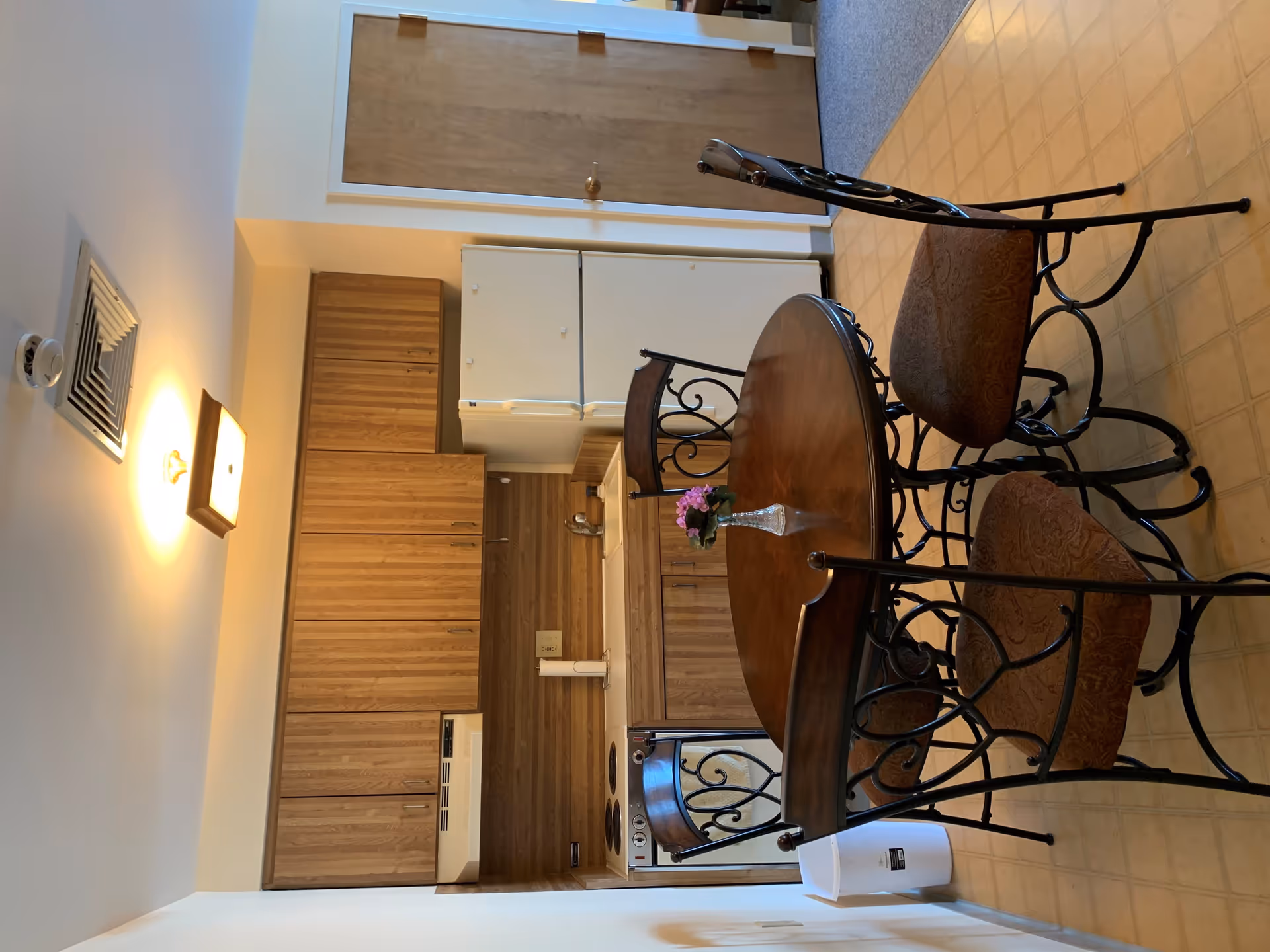 Small kitchen and dining area with a round wooden table and four metal-frame chairs in front of wood cabinets, a white refrigerator and stove.