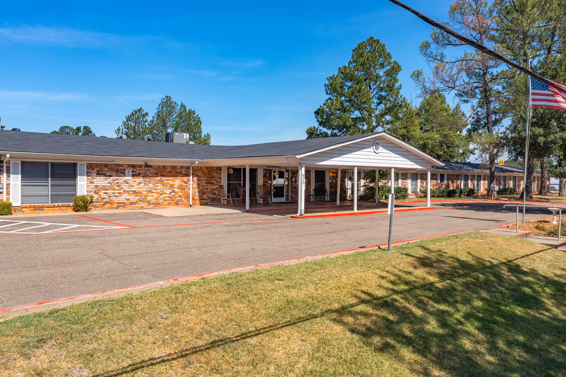 Front exterior of a one-story brick nursing facility with a covered entrance, driveway, and an American flag.