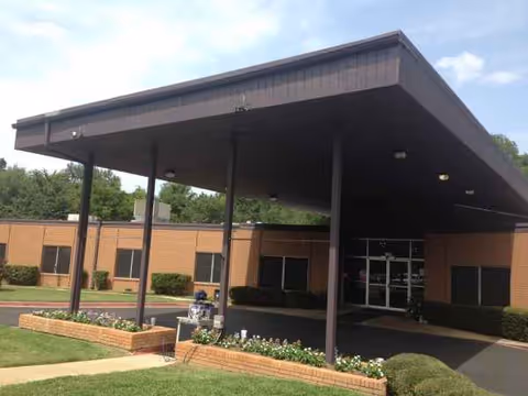 Brick senior living facility entrance with a large dark canopy and landscaped walkway.