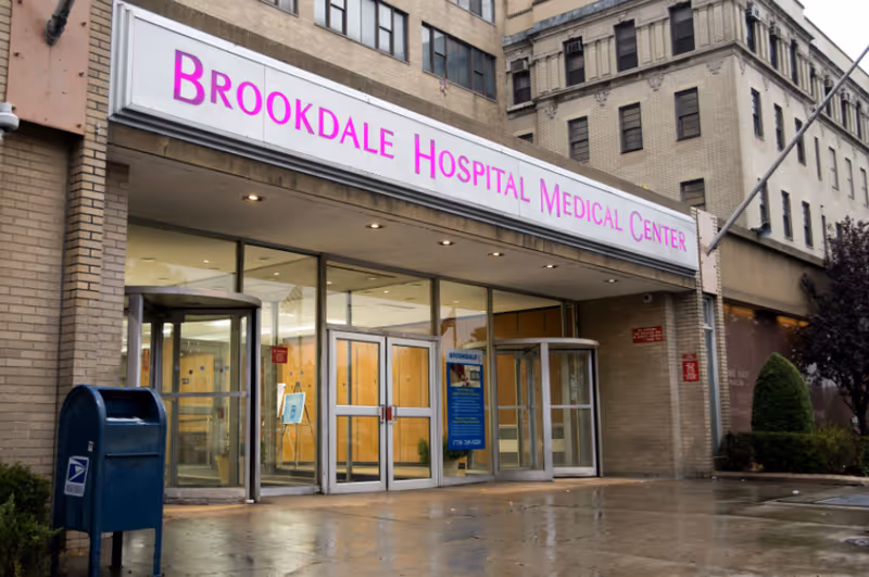 Street-level entrance of Brookdale Hospital Medical Center with glass doors, revolving doors, and a large marquee sign above.