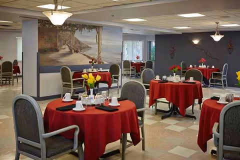 Indoor dining room in a senior facility with red-draped tables and settings.