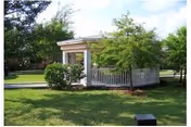 A white gazebo surrounded by green grass, trees, and shrubs in a landscaped outdoor area.