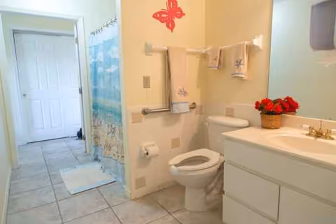Bright bathroom with toilet, sink, towels, and a shower curtain in a senior living facility.