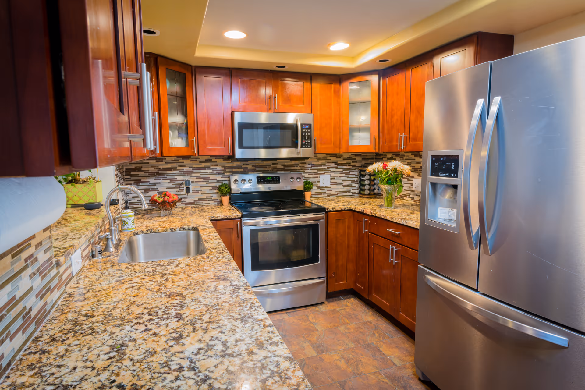 Modern U-shaped kitchen with granite countertops, stainless steel refrigerator and oven, wooden cabinets, and a sink.