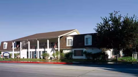 Two-story senior living building with brick facade, white columns, and landscaped front.