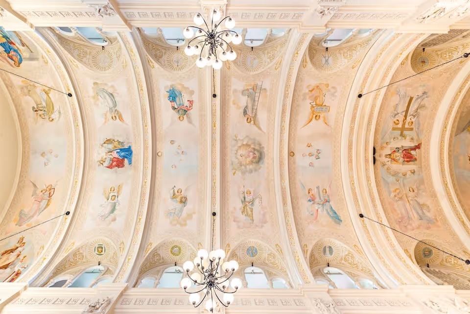 Ornate ceiling with religious-themed frescoes and two chandeliers hanging from the ceiling in a large, elegant room.