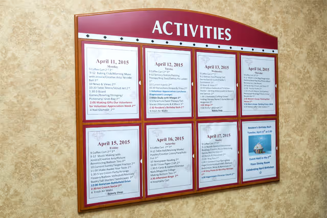 A bulletin board titled 'ACTIVITIES' displaying a weekly schedule of events and activities for residents, dated from April 11 to April 17, 2015. The board is mounted on a beige textured wall and contains printed sheets with detailed daily activity listings.