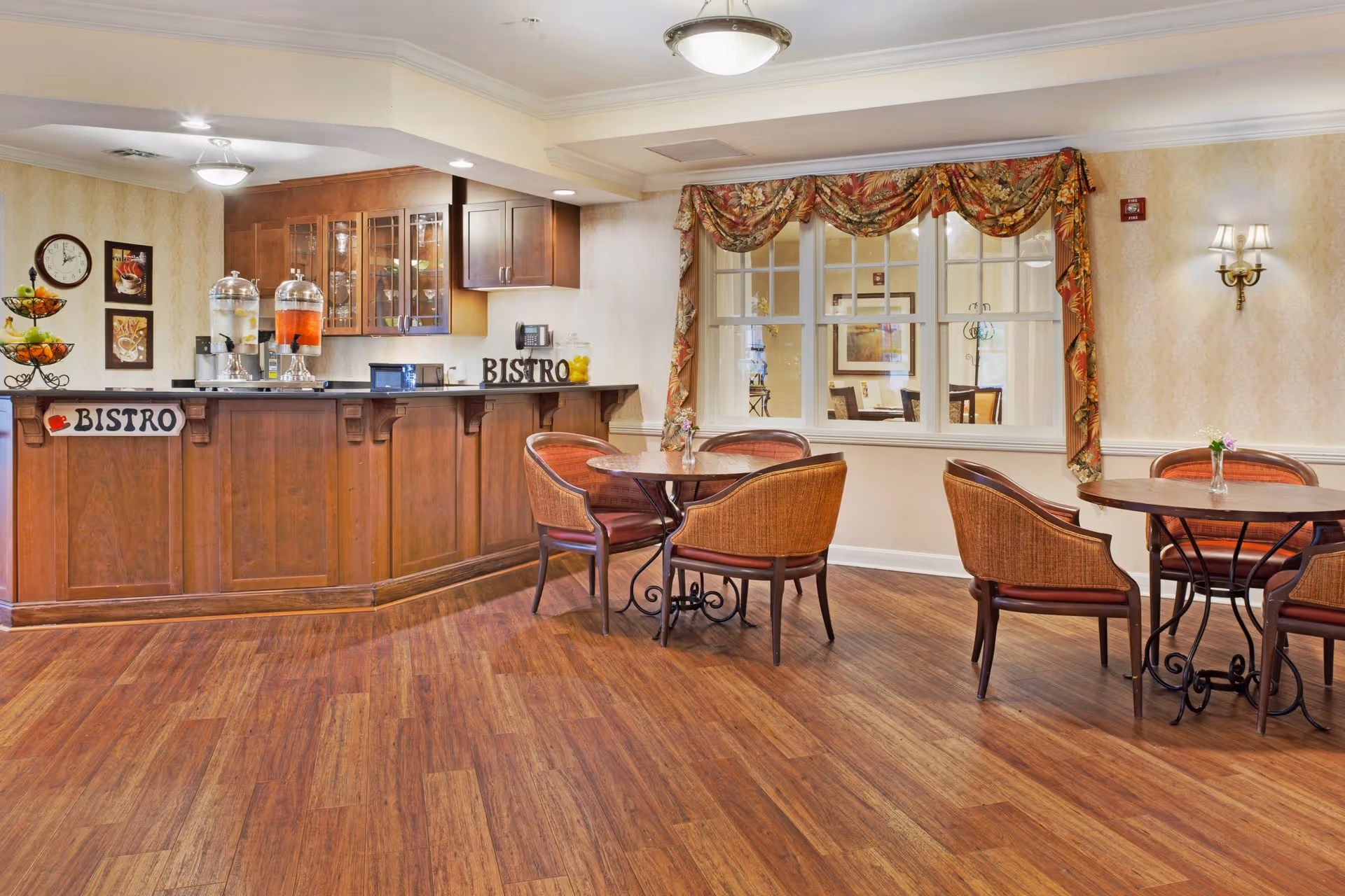 Bistro-style dining area with a wooden service counter, beverage dispensers, round tables and wicker chairs.