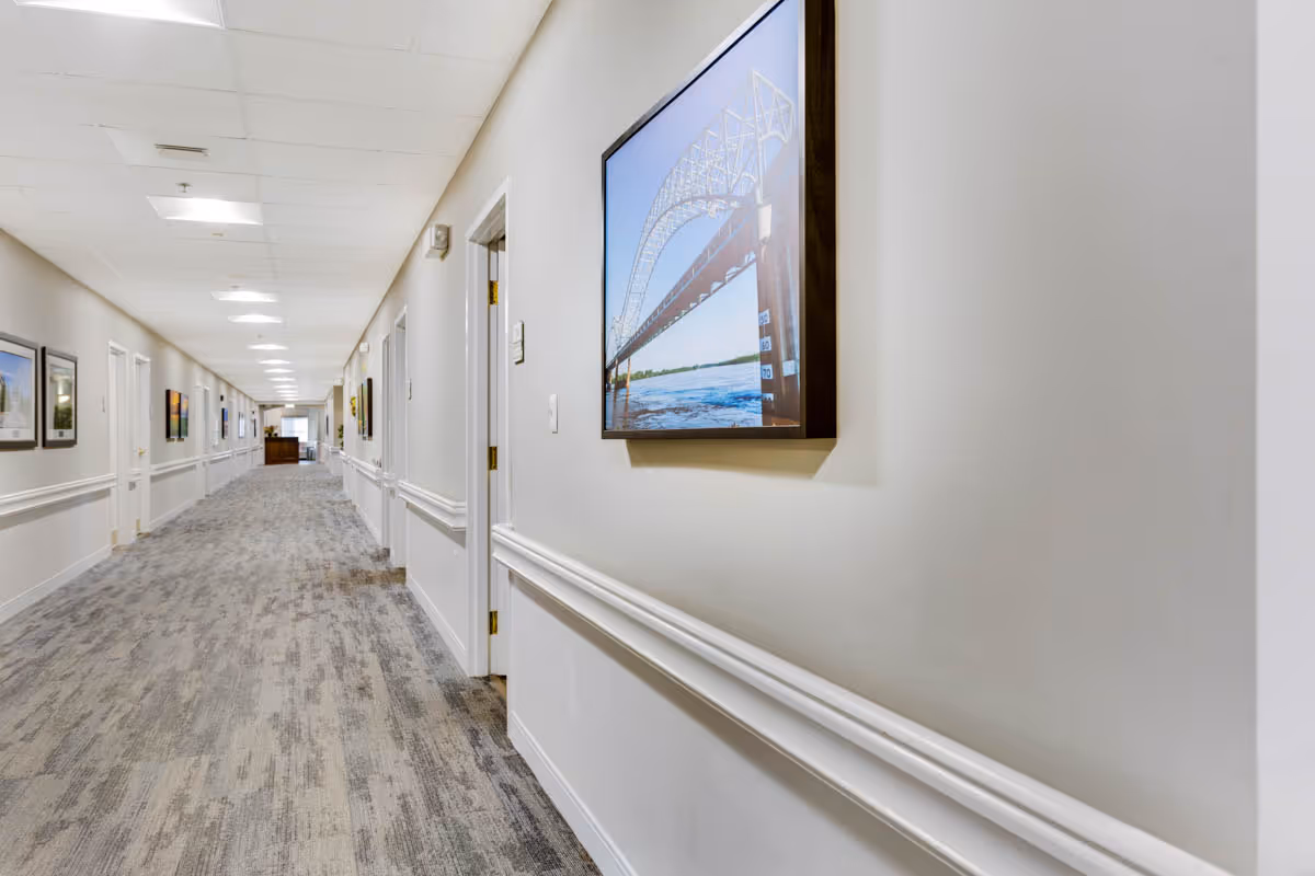 Long, well-lit interior hallway with carpeted floor, handrails and framed artwork along the walls.
