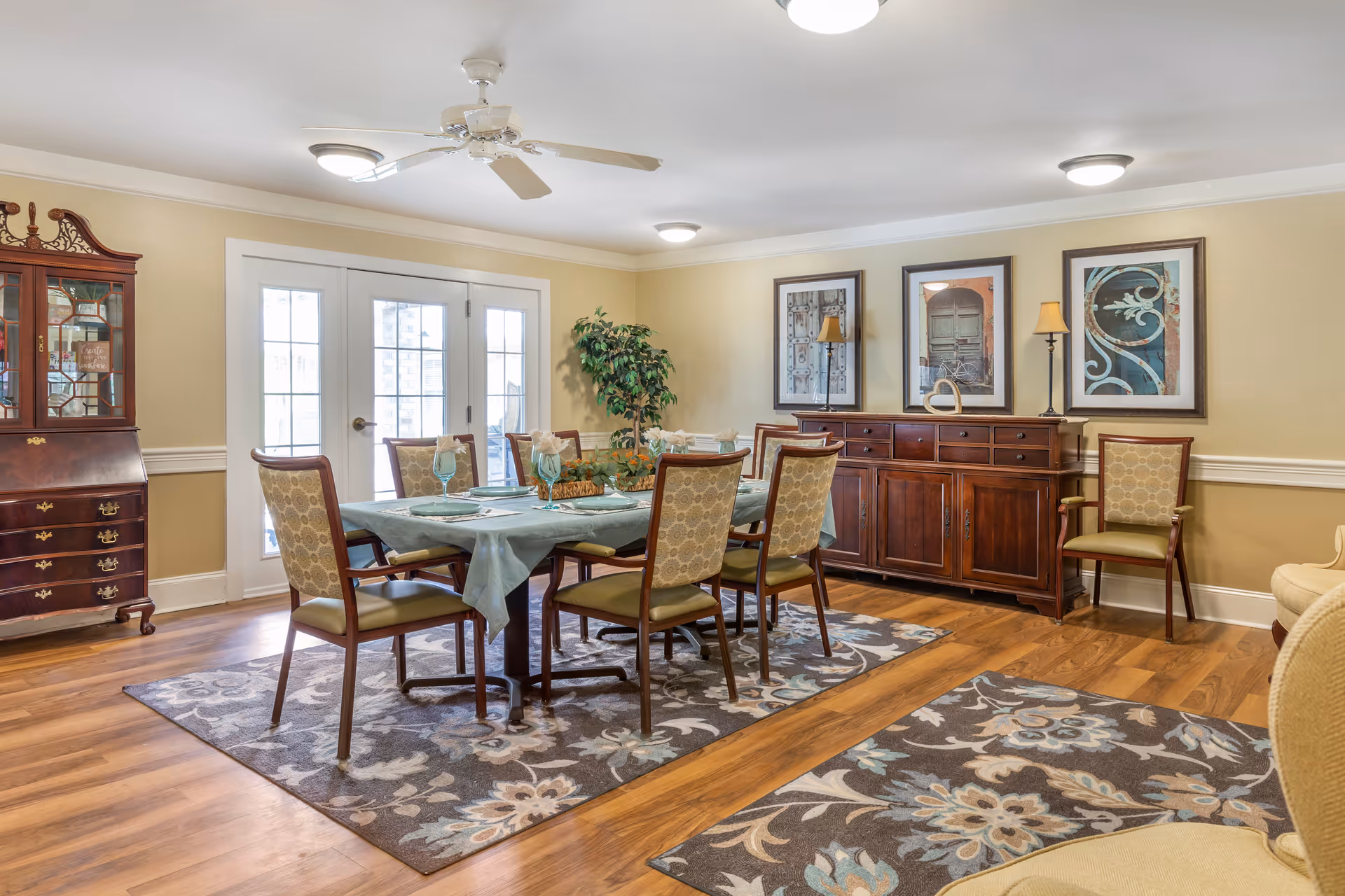Bright, well-appointed dining room with a set table, wooden sideboard, patterned rugs and French doors.