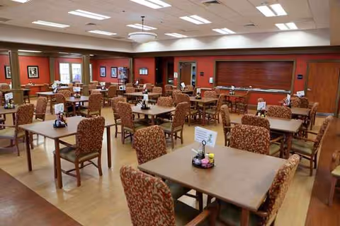 A spacious dining room in a senior living facility with many tables and chairs.